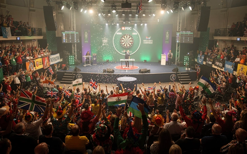 Sfeervolle zaal tijdens WK Darts met verklede fans en dartsbord